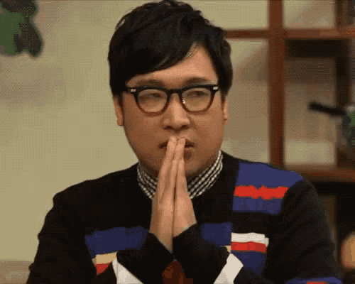 a man wearing glasses is praying with his hands folded in front of his face .