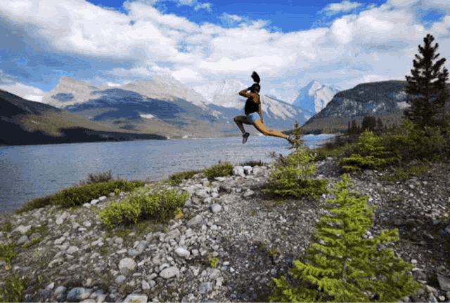 a person jumps in the air near a lake with mountains in the background