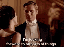 a man in a tuxedo and bow tie is talking to a woman in a dress .
