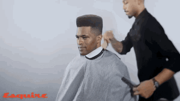 a man is getting his hair cut by a barber while wearing a striped cape .