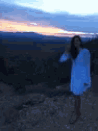 a blurry picture of a woman in a white dress standing on top of a hill at sunset .