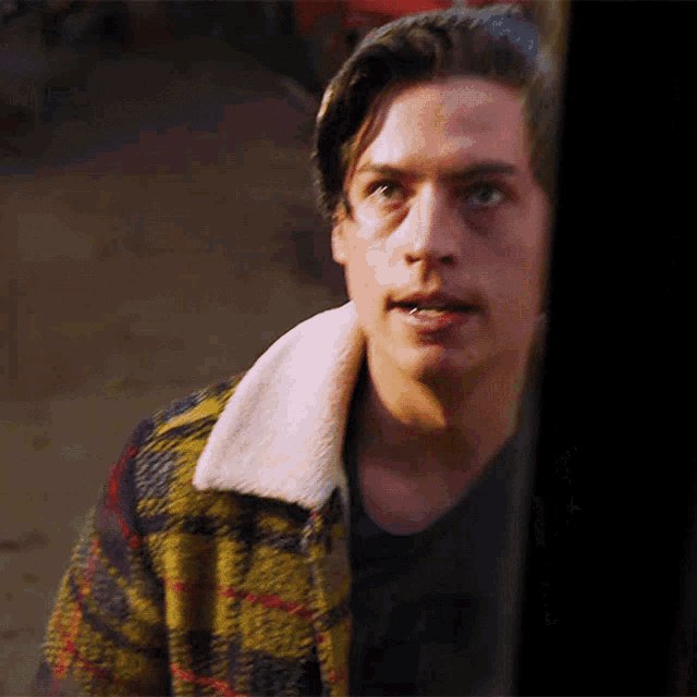 a young man wearing a plaid jacket and a black shirt with the letter t on it