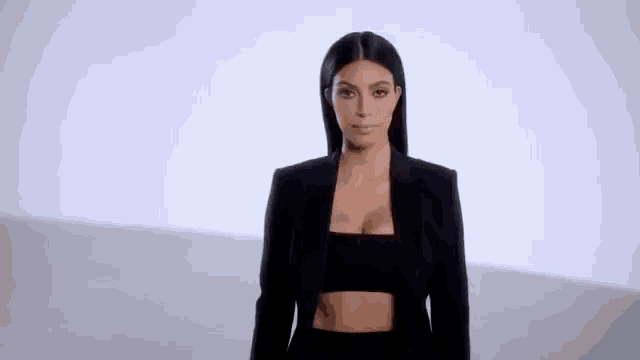 a woman in a black suit is standing in front of a white wall .