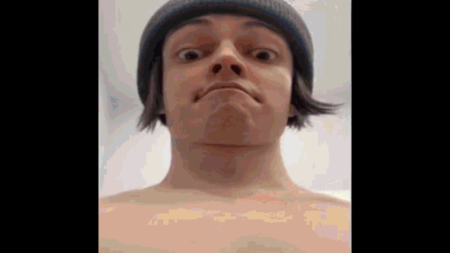 a shirtless man wearing a beanie making a funny face
