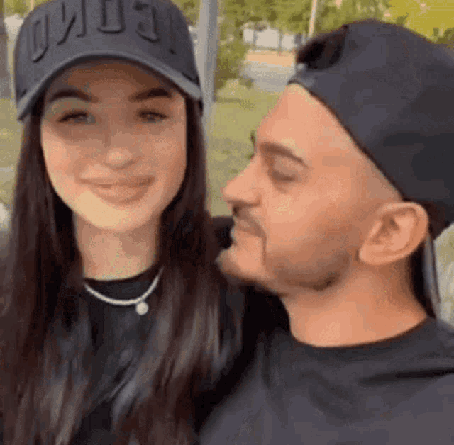 a man is kissing a woman on the cheek while wearing a black hat .