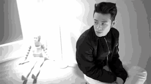a black and white photo of a man in a black jacket sitting on a chair .