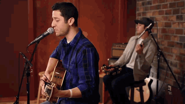 a man singing into a microphone while a woman plays guitar