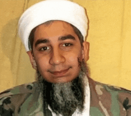 a man with a beard wearing a white turban and a camouflage jacket is smiling for the camera .