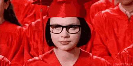 a woman wearing glasses and a graduation cap and gown is sitting in a row of graduates .