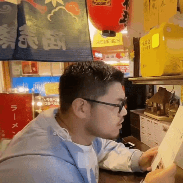 a man wearing glasses looks at a menu in front of a sign with chinese characters on it