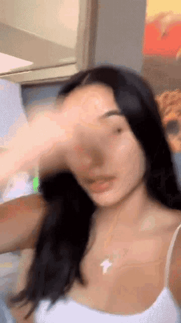 a woman is covering her face with her hand while wearing a white tank top