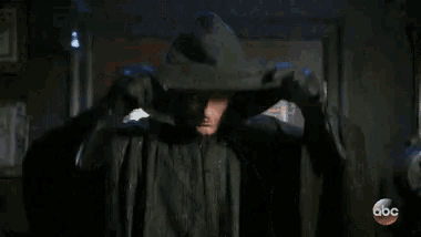 a man in a black jacket with a hood is standing in a dark room .