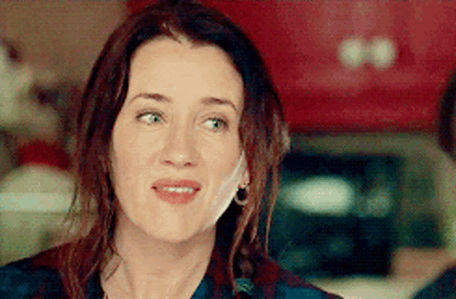 a woman wearing earrings and a plaid shirt is looking at the camera with a serious look on her face .