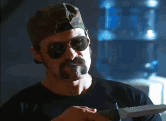 a man with a hat and sunglasses holds a knife