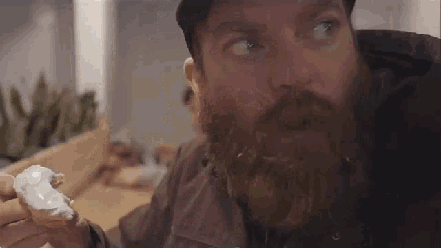 a man with a beard is eating a doughnut with icing on it .