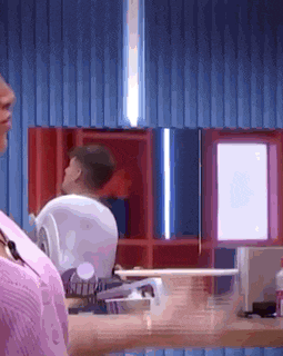 a man in a pink shirt is sitting at a desk in front of a computer monitor .