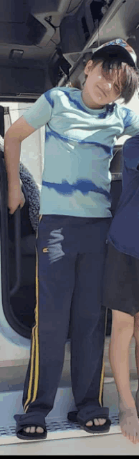 a young boy wearing a blue tie dye shirt and black sweatpants stands in front of a car door