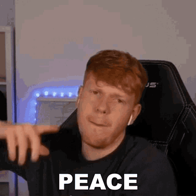 a man with red hair and a beard is sitting in a chair and pointing at the camera while saying peace .
