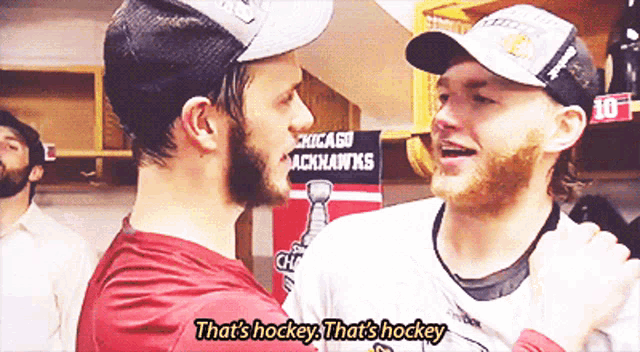 two hockey players are hugging in front of a chicago blackhawks sign