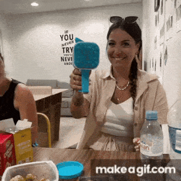 a woman is sitting at a table holding a bubble maker and smiling .