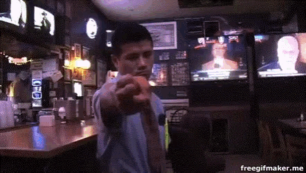 a man is pointing at the camera in a bar with a freegifmaker.me watermark on the bottom