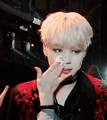 a young man with blonde hair wipes his face with a white cloth