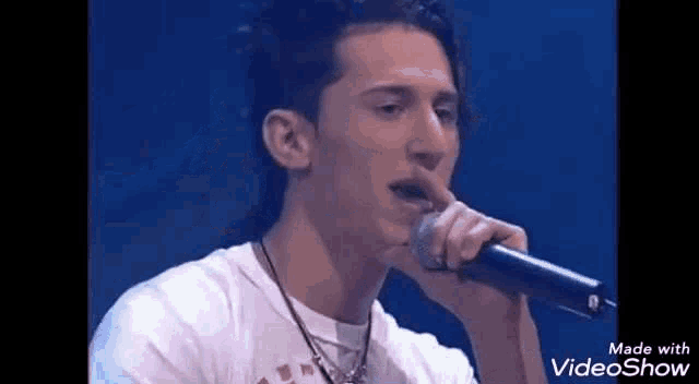 a young man is singing into a microphone while wearing a white shirt .