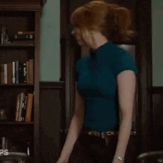 a woman in a blue shirt is standing in front of a bookcase with ps written on it