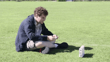 a man sits on the grass with a remote control in front of him