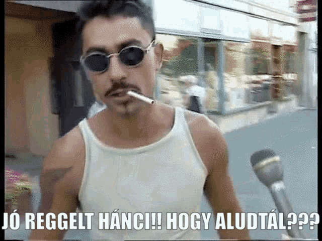 a man wearing sunglasses and a white tank top is smoking a cigarette and says jo reggelt hanci !!
