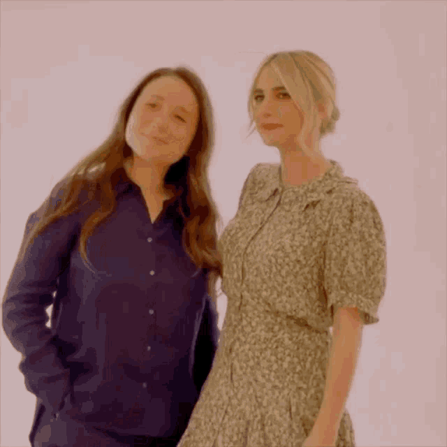 two women are standing next to each other in front of a white wall .