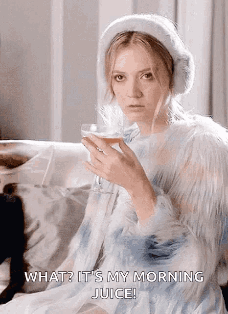 a woman sitting on a couch holding a glass of wine with the caption " what ? it 's my morning juice "