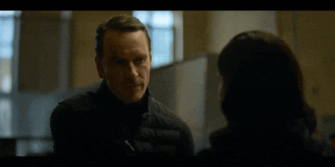 a man in a black vest is talking to a woman in a dark room