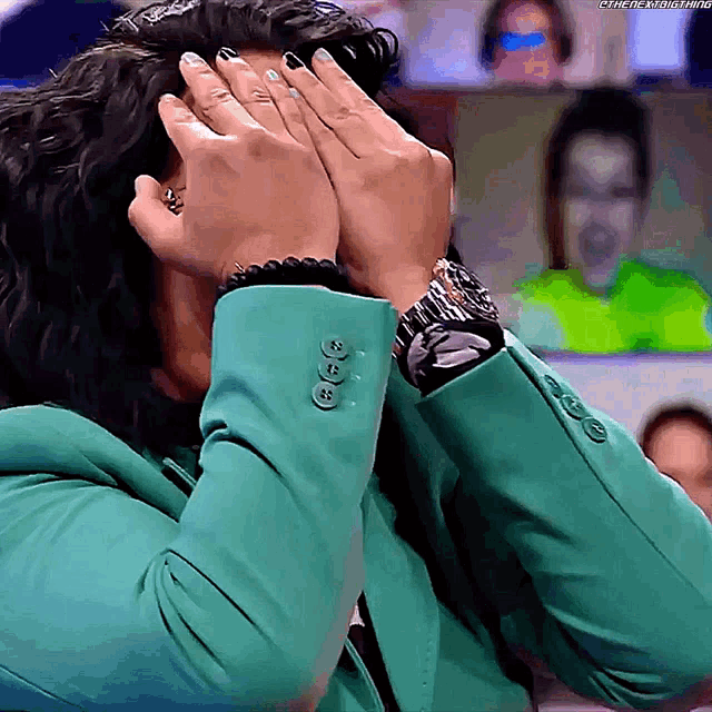 a woman in a green jacket is covering her face with her hands while wearing a watch