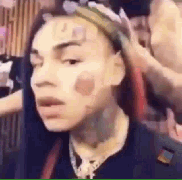 a man with a bandana on his head and a tattoo on his face is looking at the camera .