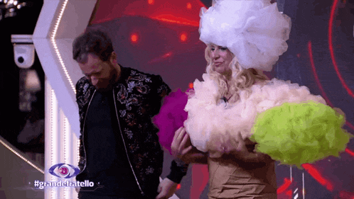 a man in a black jacket stands next to a woman in a white wig with the hashtag #granddelatello