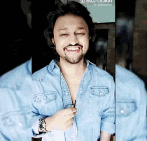 a man with a beard is smiling while wearing a denim shirt and sunglasses .