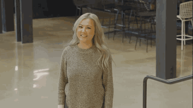 a woman in a grey sweater is standing in a room