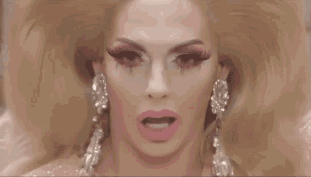 a close up of a drag queen with pink lipstick and earrings .