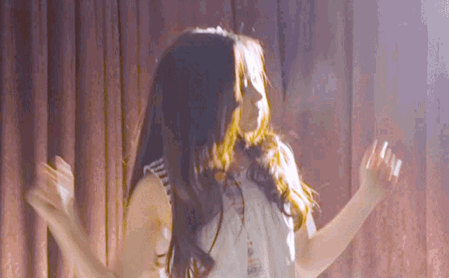 a woman with long hair is dancing in front of a pink curtain