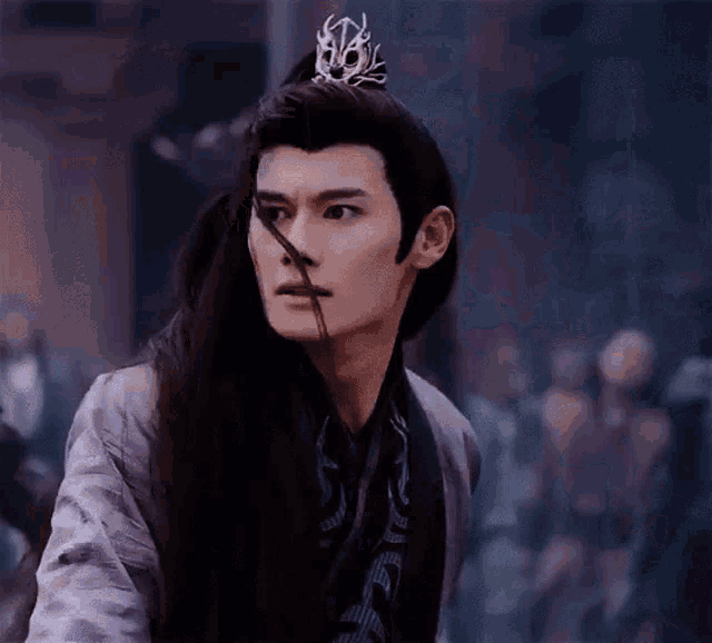 a young man with long hair and a crown on his head is standing in front of a crowd .