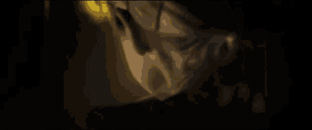 a close up of a woman 's face in a dark room with a yellow light behind her