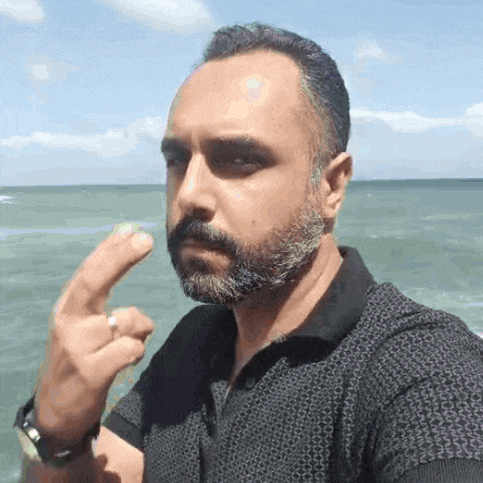 a man with a beard is giving the middle finger in front of the ocean