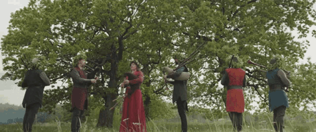 a woman in a red dress stands in a field with a group of men playing instruments