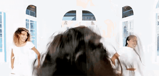 a group of women are standing around a man 's head with their hair blowing in the wind