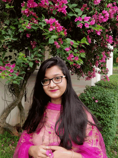 a girl wearing glasses stands in front of a tree with purple flowers