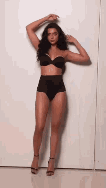 a woman in lingerie is standing in front of a white wall with her hands on her head .