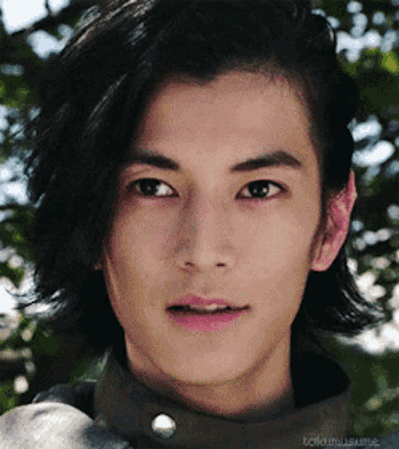 a close up of a young man 's face with a blurred background of trees