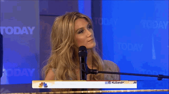 a woman singing into a microphone in front of a sign that says today