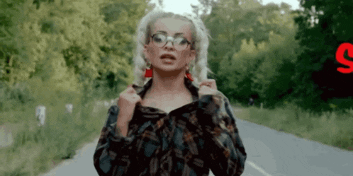 a woman wearing glasses and red earrings stands on a road